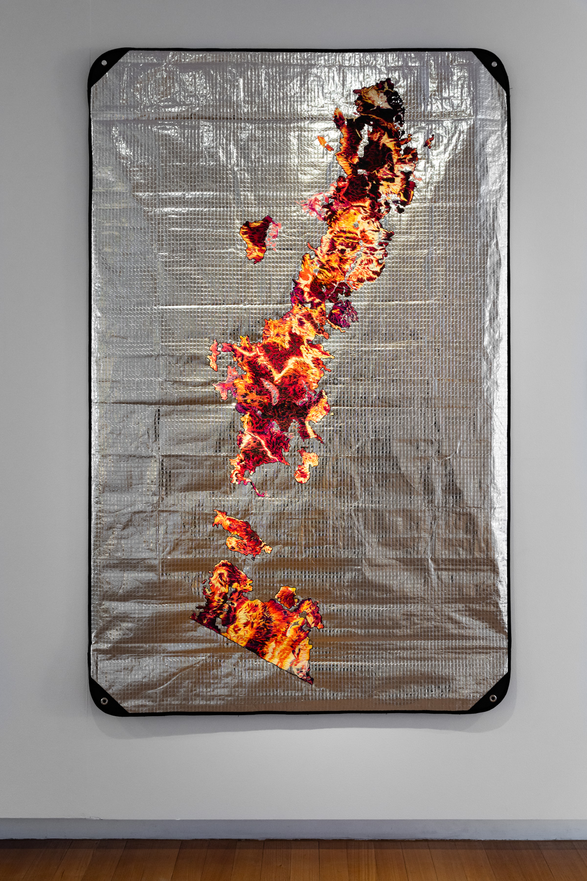 Silver emergency thermal blanket with embroidered thread that resembles maps of burnt landscapes