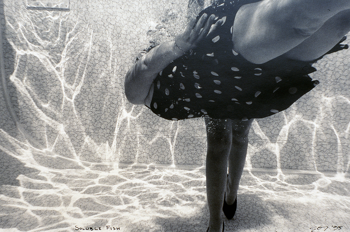 Black-and-white photograph of two people underwater in a swimming pool