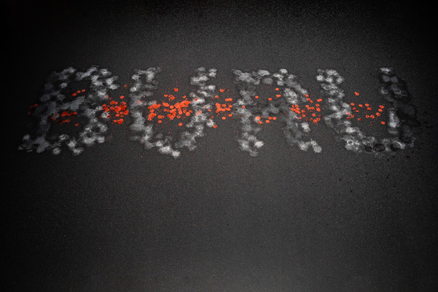 Dried drops of saltwater and iron oxide on a black platform that spell out the word 'BURU' in capital letters.