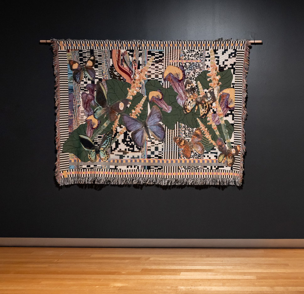 A woven tapestry depicting butterflies hanging on a dark wall in an art gallery.